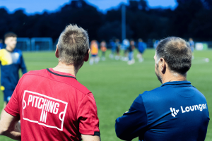 Soccer coaches watching evening training session on grassroots soccer pitch during community football development program. Entain presses soccer regulator targeting illegal gambling sponsorships Premier League clubs