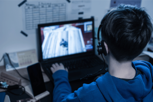 Teen playing Roblox-style online video game on laptop wearing headset amid lawsuit concerns over addictive gaming and microtransactions