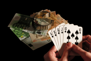 Person holding royal flush poker hand beside euro banknotes and luxury watch symbolizing gambling winnings, casino betting, and financial risk. University researchers launch major independent UK gambling harms evidence center