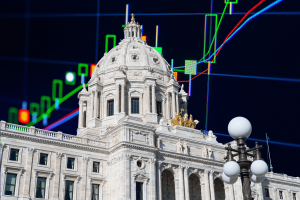 Minnesota State Capitol building in St. Paul with financial market charts and trading candlesticks overlaid, illustrating Minnesota's legal battle over prediction markets, Kalshi, Polymarket, and the state's felony ban on event-based wagering. Minnesota fights prediction market law challenges
