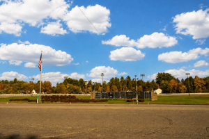 Saratoga Casino Hotel harness racing track in Saratoga Springs, New York, with scoreboard, American flag, and backstretch area under a blue sky following statewide barn fire safety review.