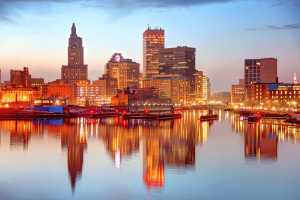Rhode Island skyline at sunset reflected on the Providence River, highlighting downtown Providence as lawmakers consider expanding the state's sports betting market and ending its sportsbook monopoly.