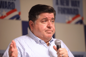 Gov. Pritzker speaking into a microphone during a public event as Illinois expands behavioral health services to recognize gambling disorder under new state law.