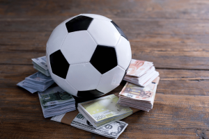 Soccer ball resting on stacks of euro and U.S. dollar banknotes, illustrating sports betting, match-fixing, gambling integrity risks, and athlete betting regulations. Norway match-fixing survey shows sports manipulation reporting gaps amid global integrity concerns