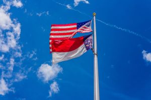 The USA and North Carolina flags flying in front of a blue sky.