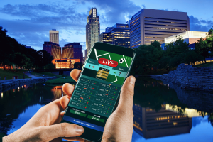 Online sports betting app displayed on a smartphone against the Omaha, Nebraska skyline.