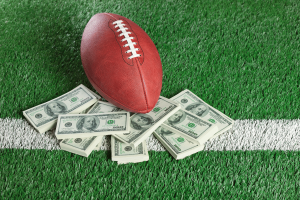 American football on stacks of dollar bills on a field, illustrating NFL betting and prediction market growth.
