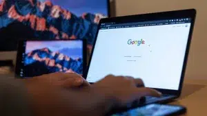 A person using a laptop displaying the Google search homepage.
